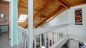 Ein Zimmer mit schrägverdeckter Holzbalkendecke, einer Treppe und Blick auf eine untere Ebene.