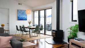 A modern living room with a dining area, a black wood-burning stove, and a large window.