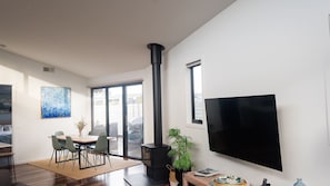 A modern living room with a black wood-burning stove, a flat-screen TV, and a dining area with a table and chairs.