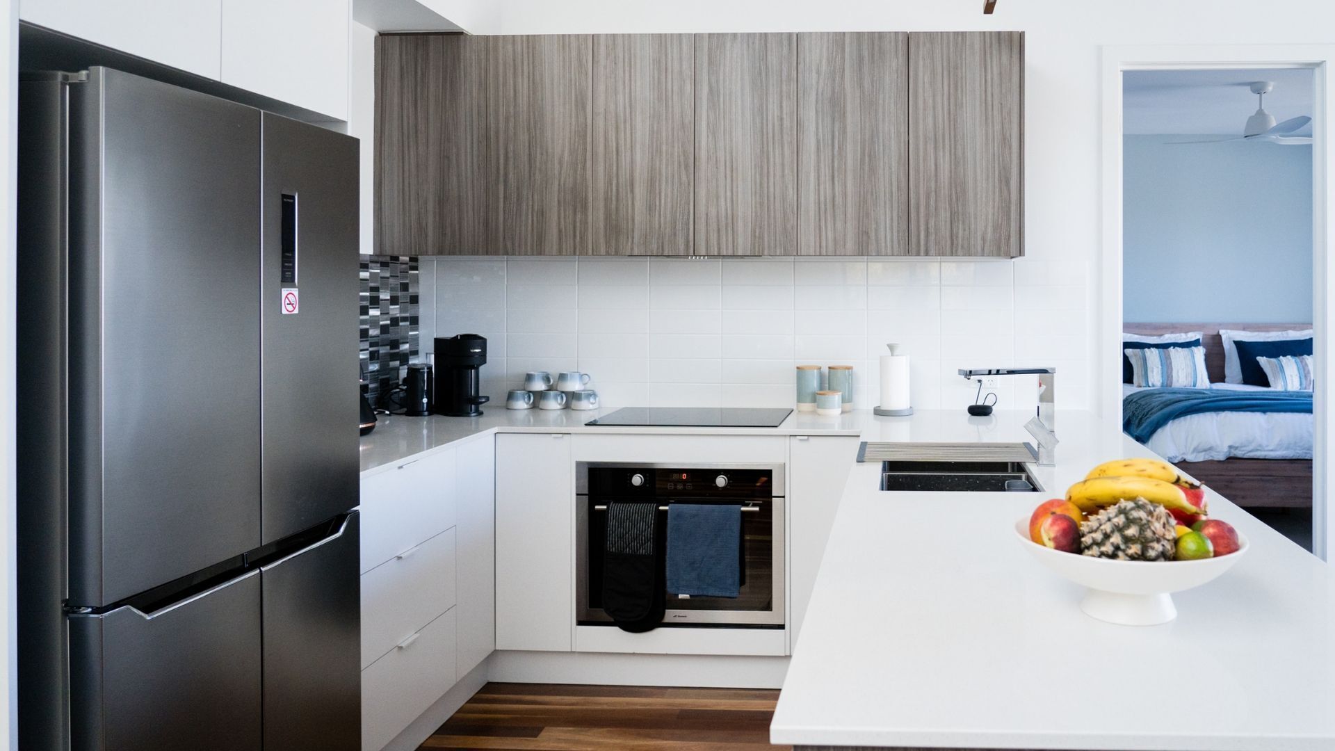 A modern kitchen with a built-in oven, a refrigerator, and a dining area with a fruit bowl.