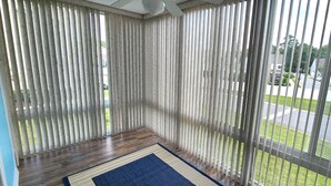 Een balkon met verticale zonwering, een houten vloer en een blauw vloerkleed.