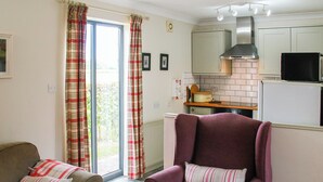 A living room with a sofa, a purple armchair, and a kitchen area with a stove, microwave, and cabinets. - 2 bedroom accommodation in Terrington St Clements, near King&rsquo;s Lynn (Terrington St Clements, near King&rsquo;s Lynn)