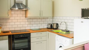 A compact kitchen with white cabinets, a stainless steel range hood, a built-in oven, a microwave, a sink with a green mat, and a washing machine. - 2 bedroom accommodation in Terrington St Clements, near King&rsquo;s Lynn (Terrington St Clements, near King&rsquo;s Lynn)