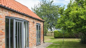 A brick house with large sliding glass doors, a red-tiled roof, and a grassy yard with a hedge and a tree. - 2 bedroom accommodation in Terrington St Clements, near King&rsquo;s Lynn (Terrington St Clements, near King&rsquo;s Lynn)
