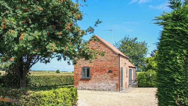 A small brick building with a gravel driveway, surrounded by greenery and a clear sky. - 2 bedroom accommodation in Terrington St Clements, near King&rsquo;s Lynn (Terrington St Clements, near King&rsquo;s Lynn)