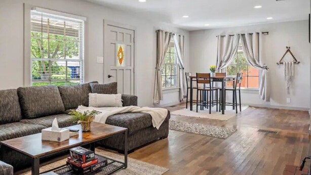 A spacious living room with a dark grey sofa, a wooden coffee table, and a dining area with a table and chairs.