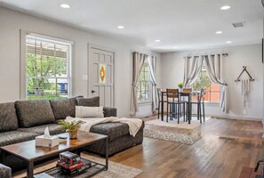 A spacious living room with a dark grey sofa, a wooden coffee table, and a dining area with a table and chairs.