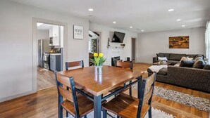 A modern living room with a wooden dining table, a sofa, and a TV mounted on the wall.