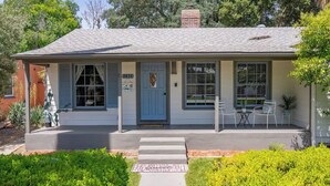 A single-story house with a front porch, a blue door, and a small patio with chairs.