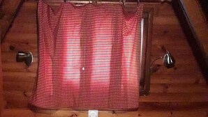A cozy attic bedroom with wooden walls, two beds with floral bedding, a small wooden nightstand, and a red and white checkered curtain. - CHALETS MONTAGNARD (Jausiers)