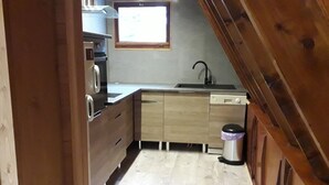 A compact kitchen with wooden cabinets, a sink, and a window above the countertop. - CHALETS MONTAGNARD (Jausiers)