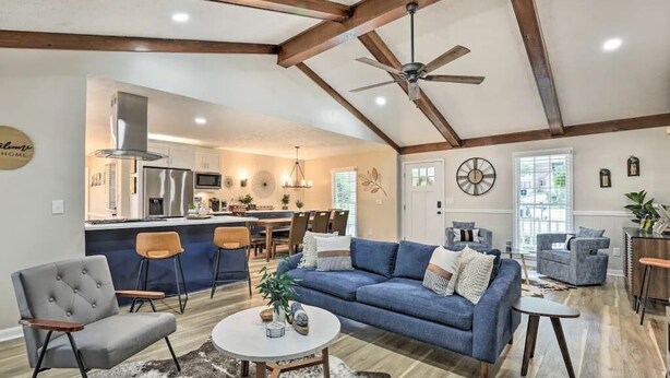 A spacious living area with a blue sofa, a grey armchair, and a coffee table. There is a kitchen in the background with a bar and a dining area. - Chic Lilburn Getaway w/Media Room + Fire Pit (Lilburn)
