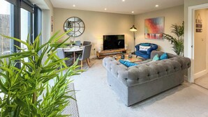 Ein modernes Wohnzimmer mit einem grauen Sofa, einem Esstisch mit Stühlen, einem Fernseher und einem großen Fenster.