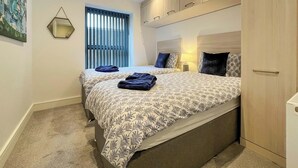 Ein Schlafzimmer mit zwei Betten, einem Fenster mit Jalousien, einem Bild an der Wand und einem Kleiderschrank.