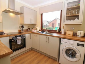 Una cocina compacta con horno integrado, lavadora y ventana con vistas a casas.