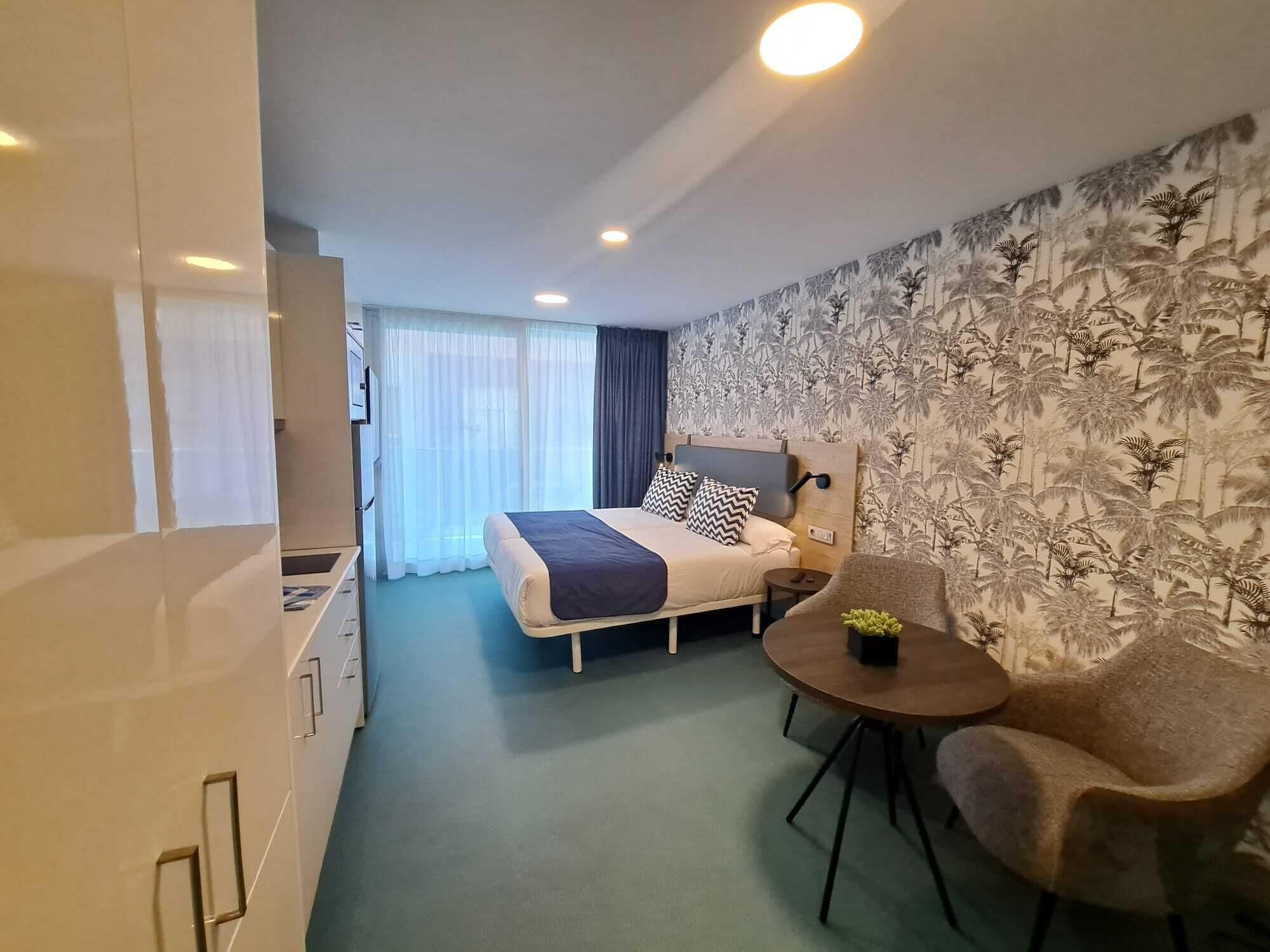 A hotel room with a bed, a small table, a chair, a desk, and a window with curtains.