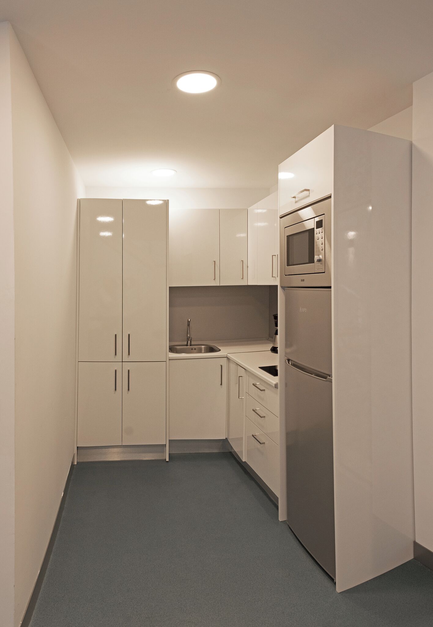 A compact kitchen with white cabinets, a stainless steel refrigerator, and a microwave.