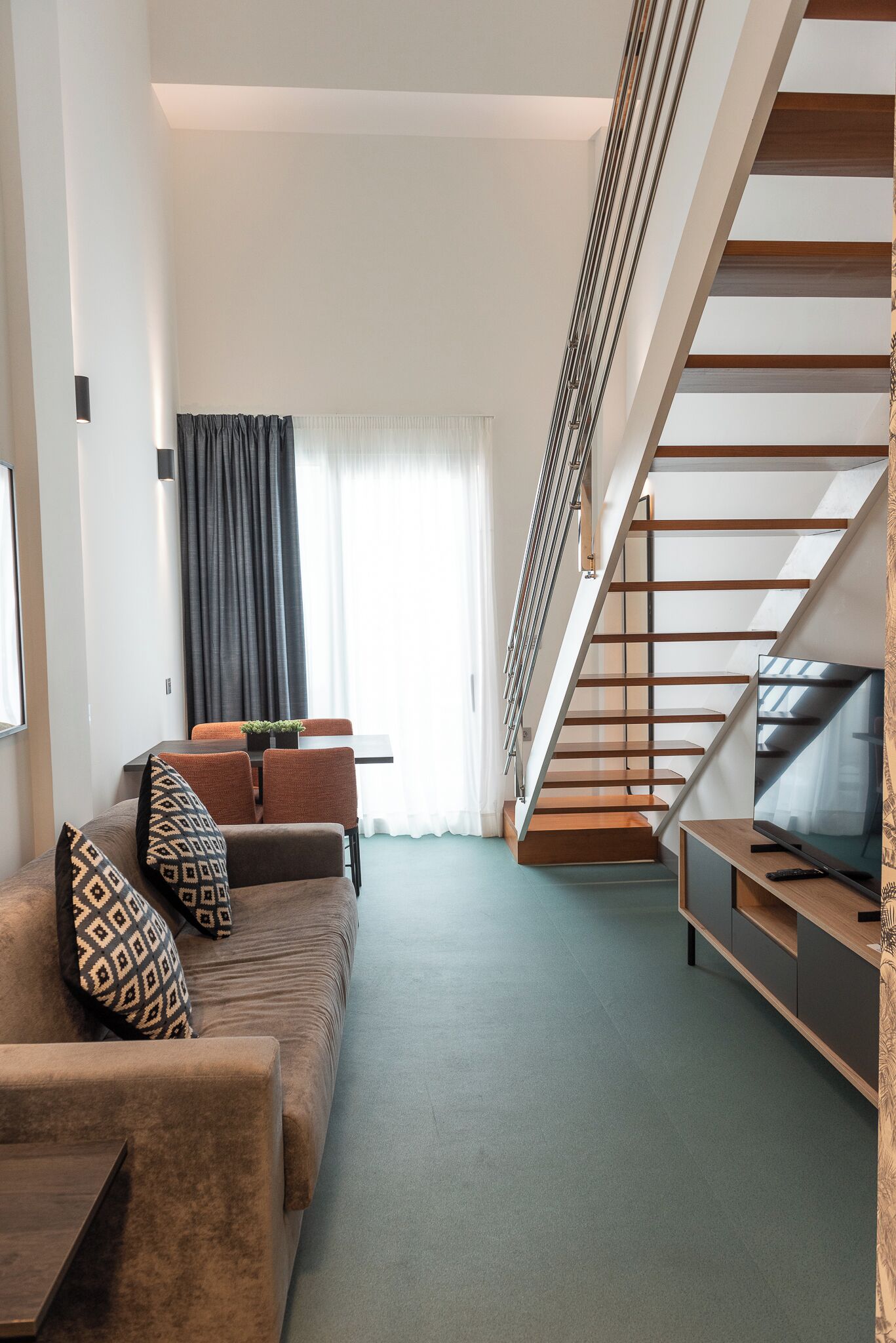 A modern living room with a sofa, a dining table, and a staircase.