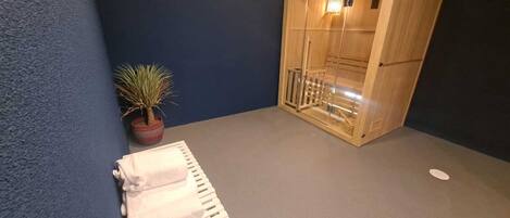 Zona de spa con sauna de madera, una planta pequeña en maceta y un perchero blanco.
