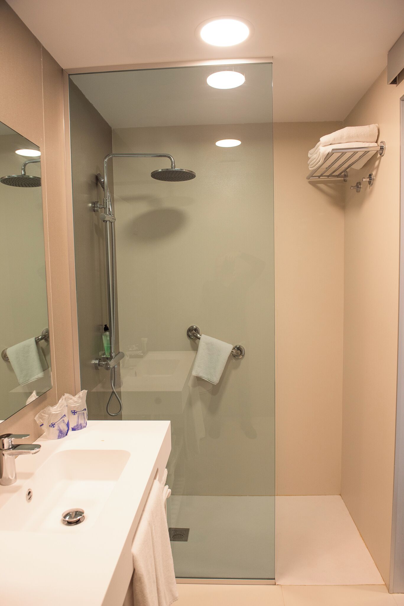 Ein modernes Badezimmer mit einer Glaskabine zur Dusche, einem weißen Waschbecken mit Spiegel und einem Handtuchhalter.