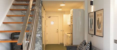 Un interior moderno con una escalera, una sala de estar con sofá y sillones, y una mesa de comedor.