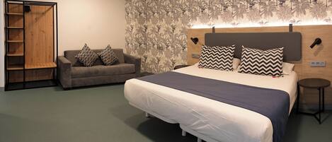 A bedroom with a bed, a sofa, a wardrobe, and a wall with a tropical wallpaper.