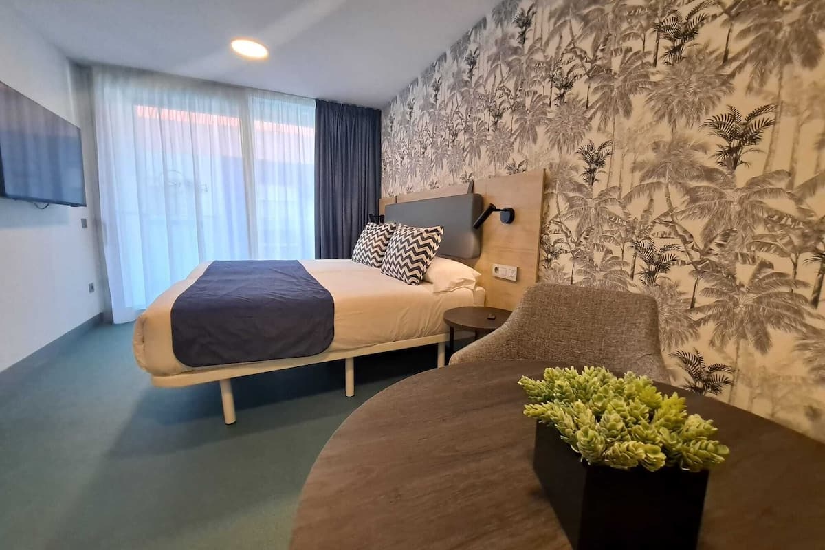 A hotel room with a bed, a bedside table, a chair, and a wall-mounted TV.