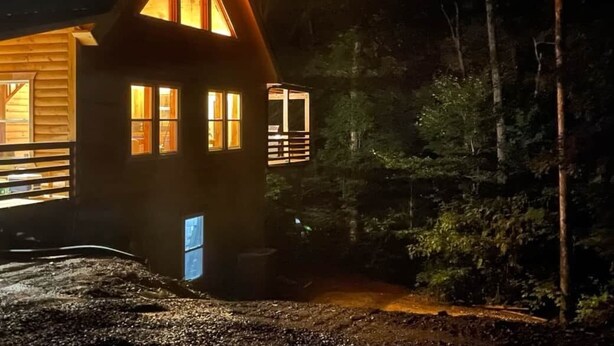 A wooden cabin with multiple windows and a small attached structure, surrounded by dense forest. - Windrock Ridge Luxury Ethan Cabin: Ride-In Access, Sleeps 16. (oliver spring)