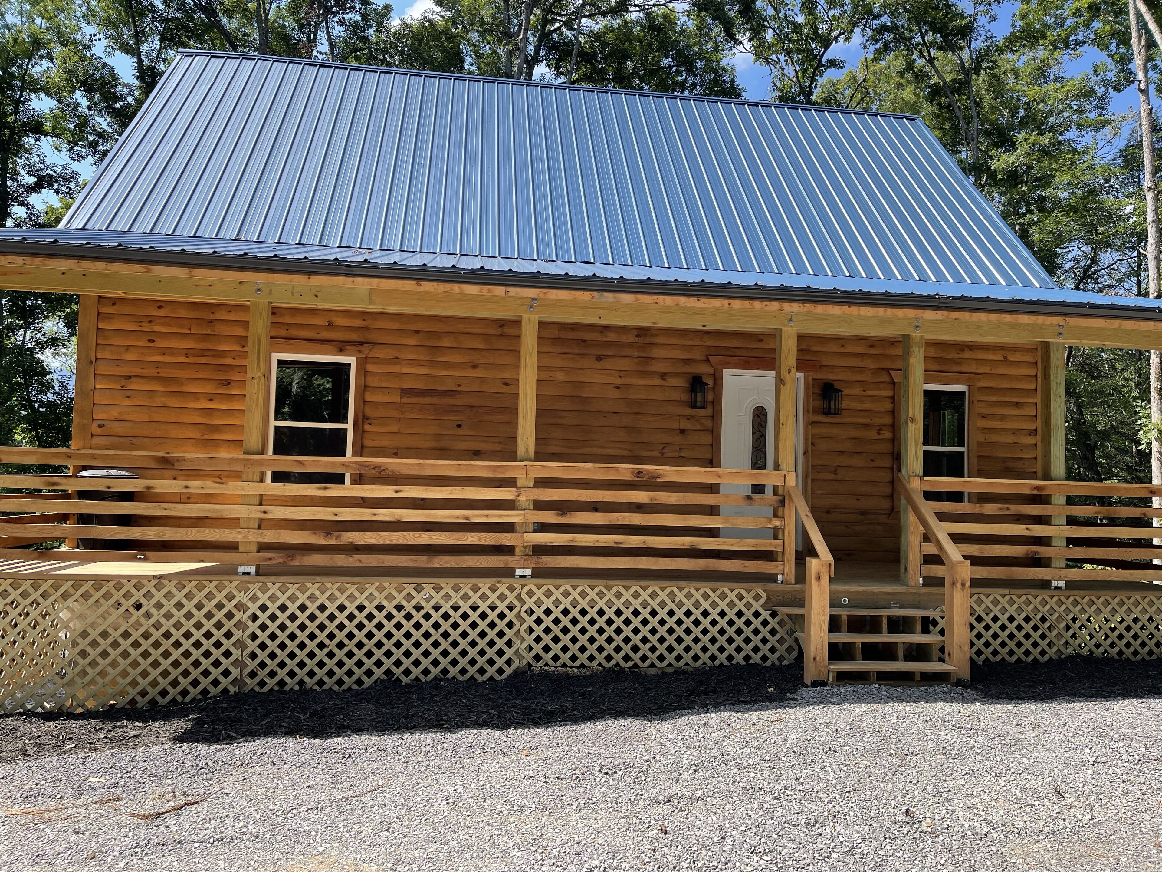 A wooden cabin with a metal roof, a porch with wooden railings, and a lattice fence.