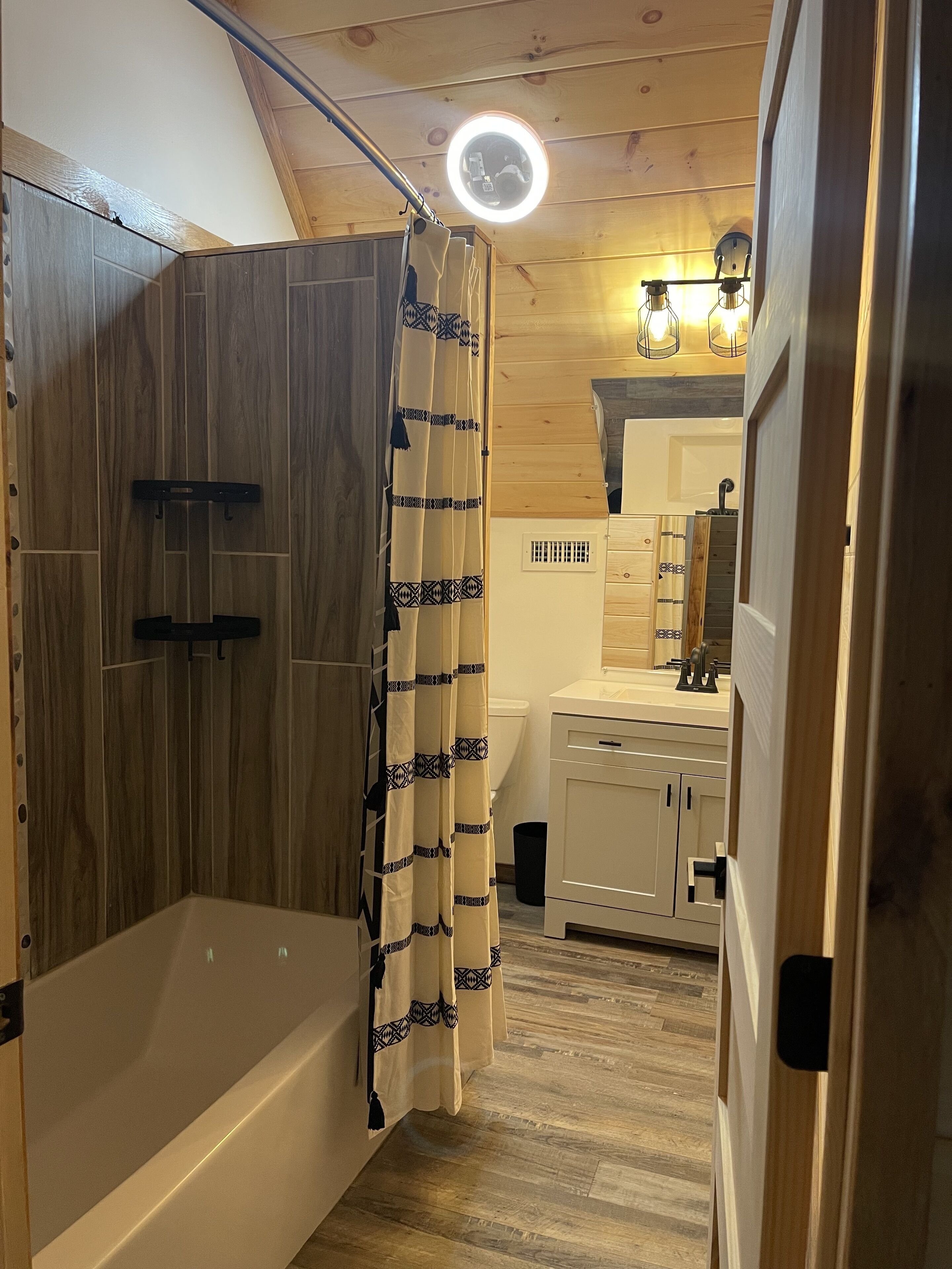 A wooden cabin bathroom with a bathtub, shower curtain, and a vanity with a mirror.
