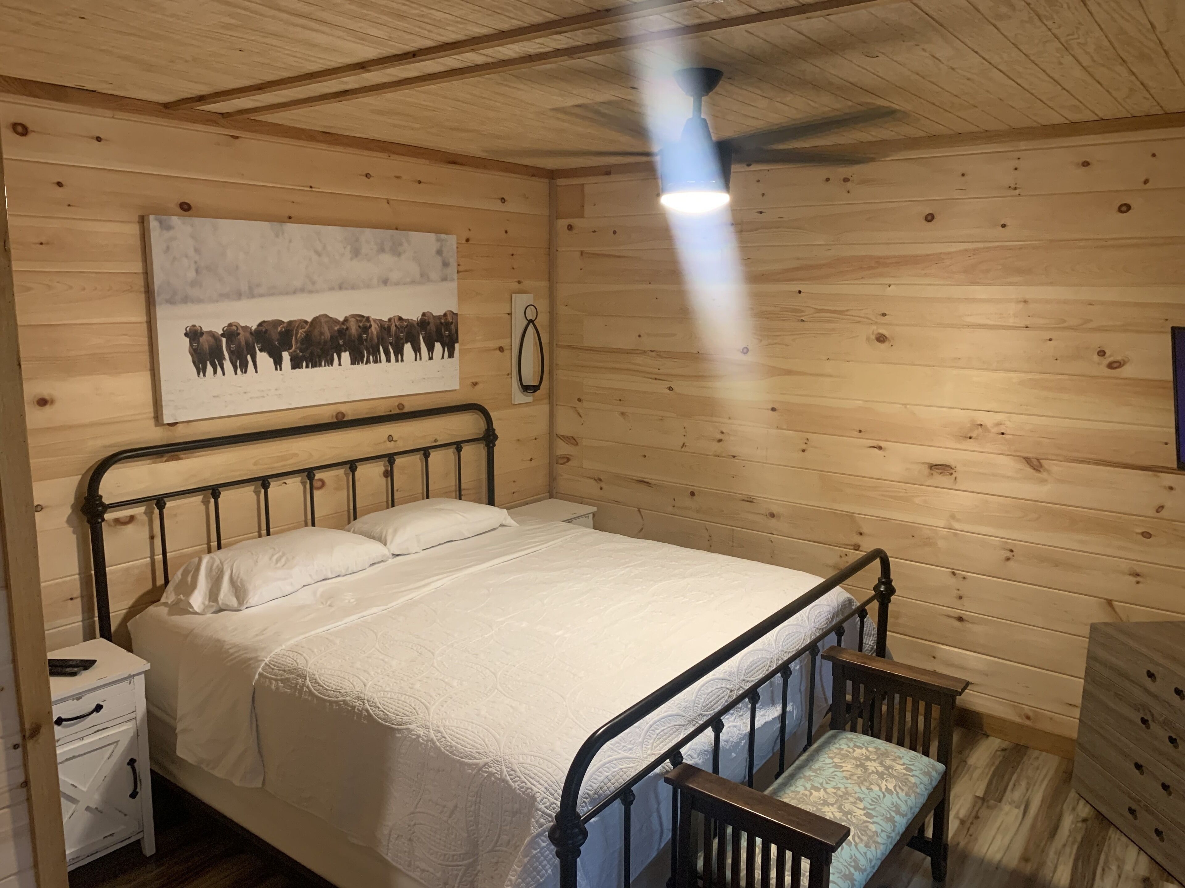 A wooden cabin bedroom with a bed, a nightstand, a bench, and a ceiling fan.