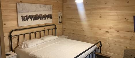 A wooden cabin bedroom with a bed, a nightstand, a bench, and a ceiling fan.