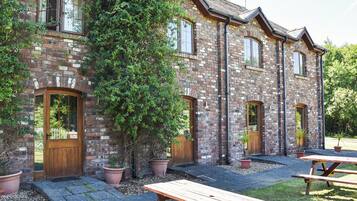 A brick building with multiple doors and windows, surrounded by potted plants and picnic tables.