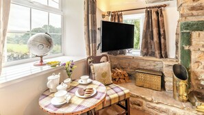 A cozy room with a stone fireplace, a television, a globe, and a table set with tea cups and pastries.