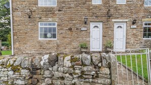 A stone building with multiple windows and doors, a stone wall in front, and a small garden area.