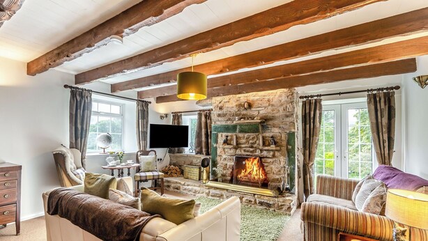 A cozy living room with exposed wooden beams, a stone fireplace, a comfortable sofa, and a television.