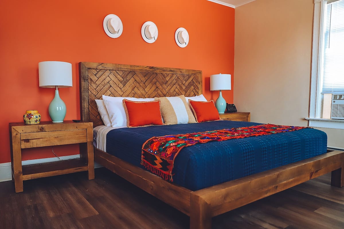 Un dormitorio con cama de madera, paredes anaranjadas y ventana con persianas.