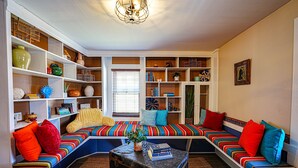Una sala de estar acogedora con un banco integrado, rodeada de estanterías llenas de libros y objetos decorativos.
