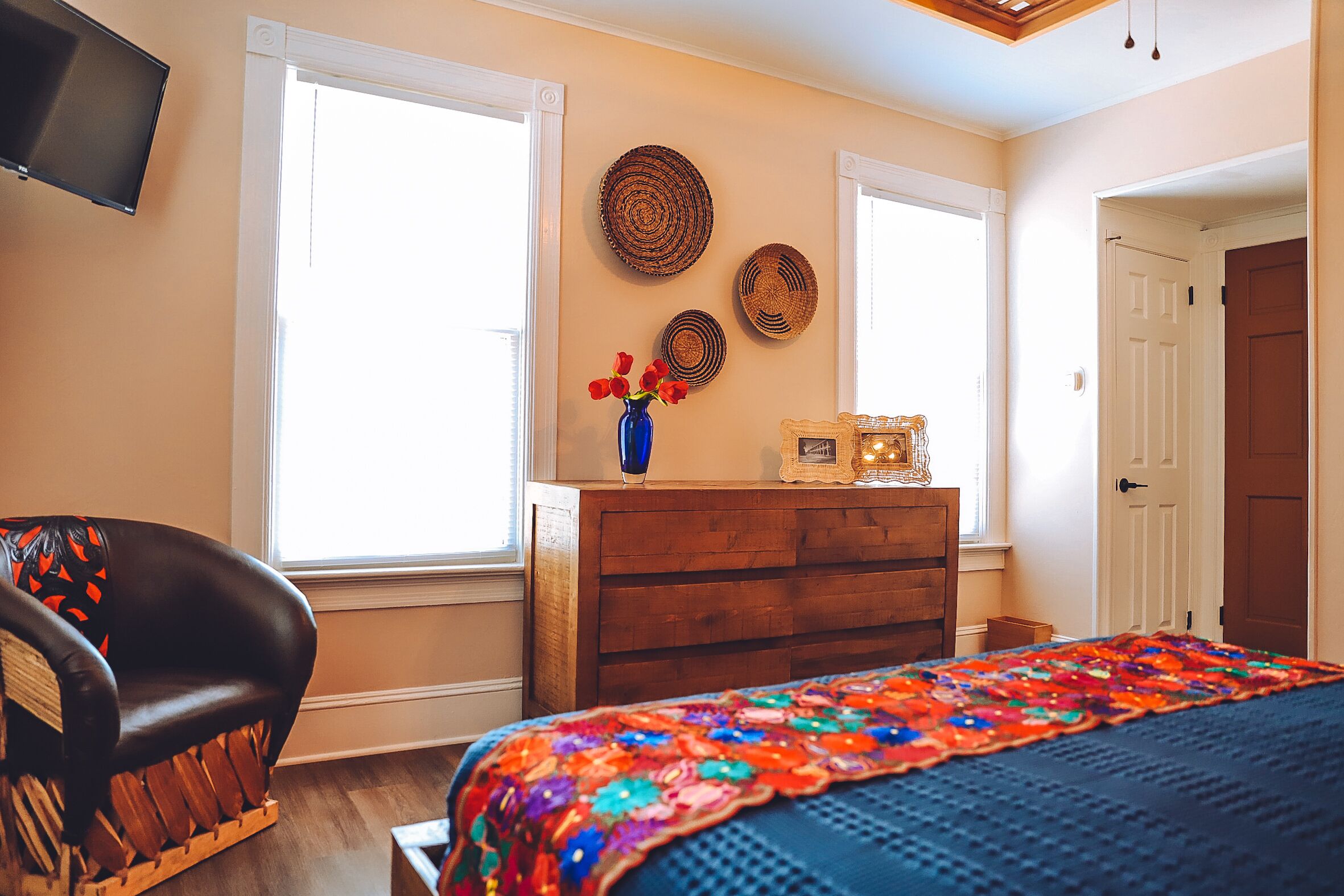 A bedroom with a bed, a wooden dresser, a chair, and a TV mounted on the wall.