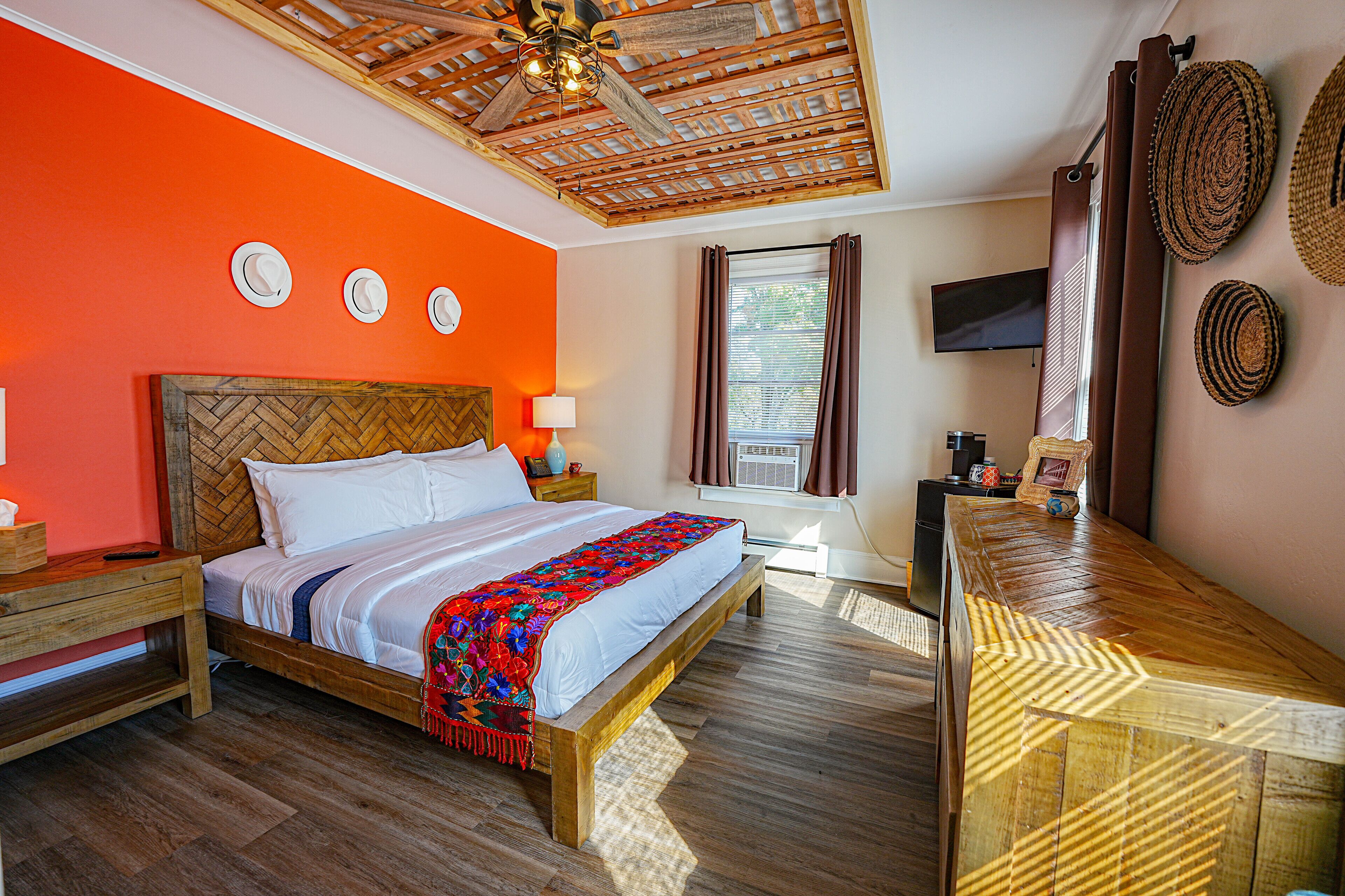 A bedroom with a wooden bed, a wooden headboard, a wooden bench, a television, and a window with curtains.