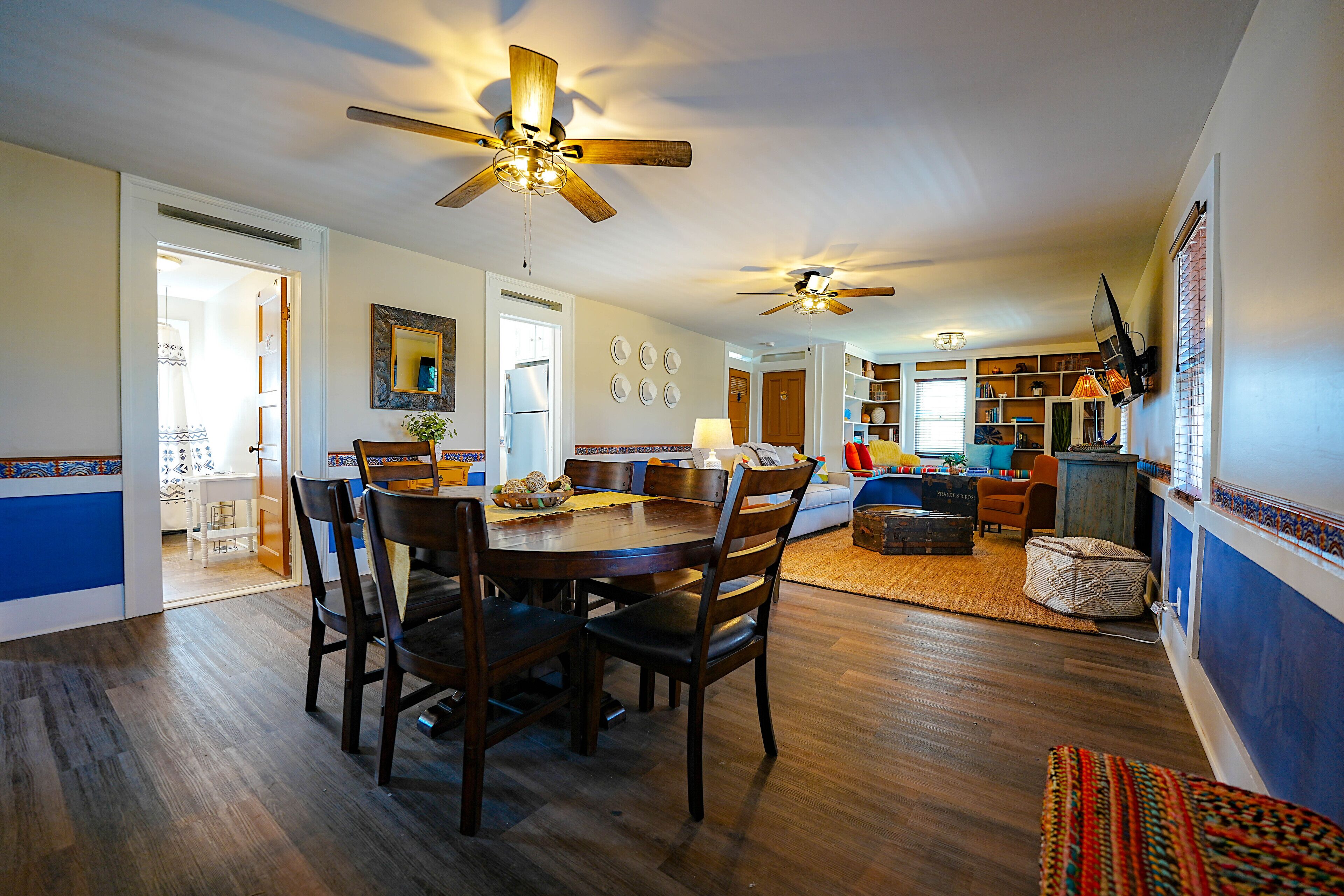 A spacious dining area with a wooden table and chairs, a ceiling fan, and a kitchen in the background.