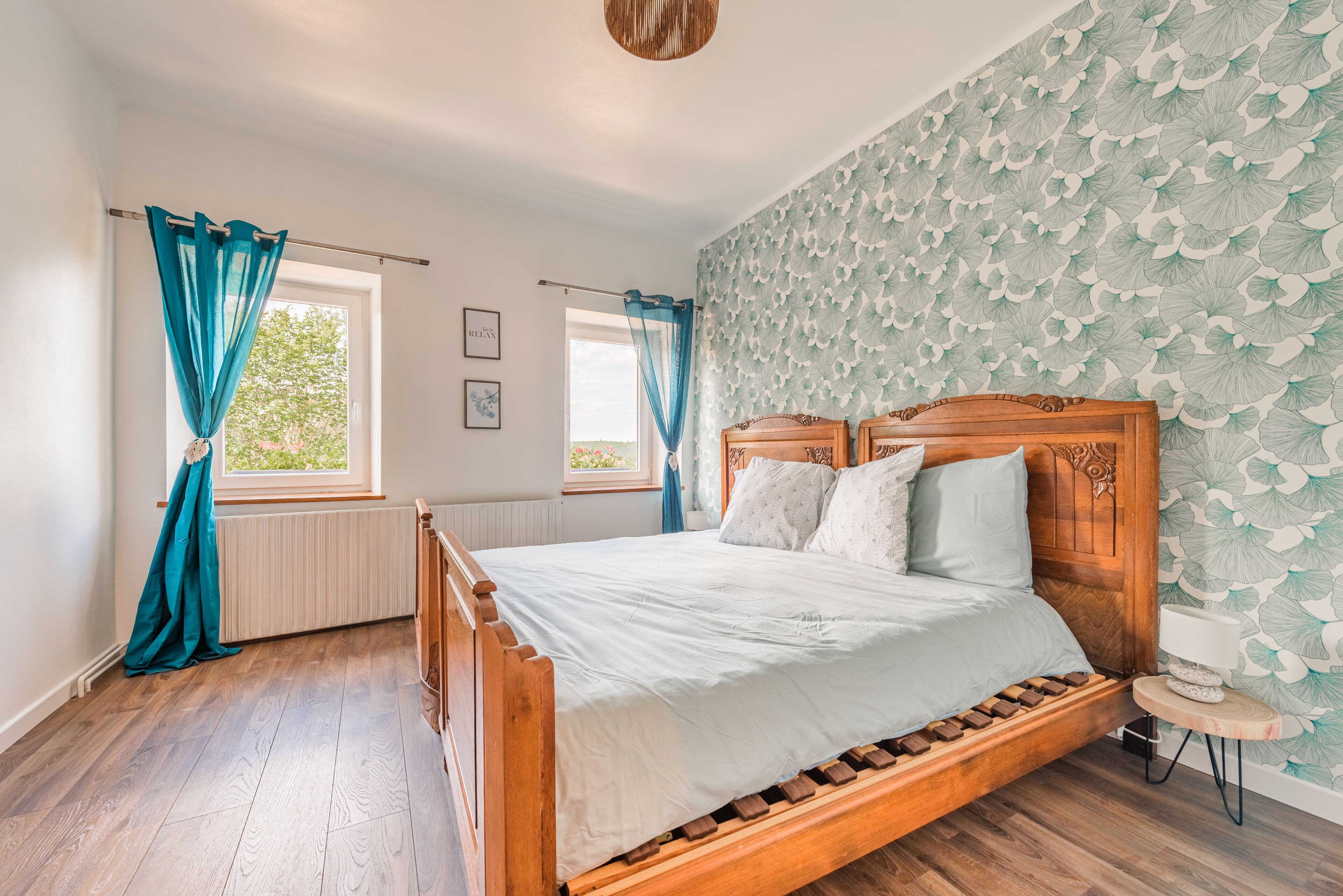A bedroom with a wooden bed, a window with curtains, a radiator, and a patterned wallpaper.