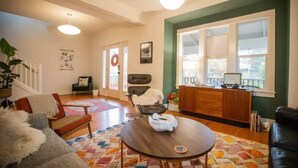 A living room with a sofa, a coffee table, a chair, a rug, a desk with a computer, and a window with blinds. - Alberta Arts District 2 private bedrooms/bathroom (Portland)