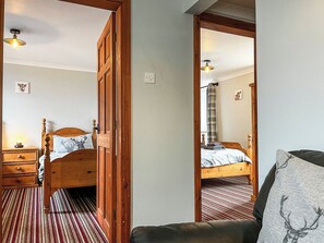 A bedroom with a wooden bed, a nightstand, a chair, a mirror, and a striped carpet. - Haddon Cottage - UK40270 (Bakewell)