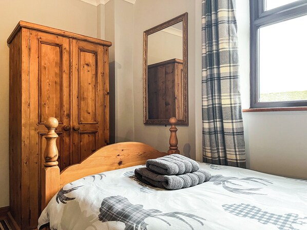A bedroom with a wooden wardrobe, a bed with a patterned duvet, a mirror, and a window with curtains.