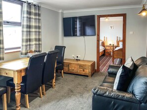 A room with a dining table, chairs, a sofa, a TV, and a bed.