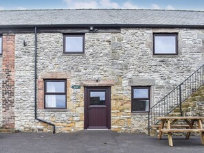 A stone building with a wooden door, two windows, and a staircase. - Haddon Cottage - UK40270 (Bakewell)
