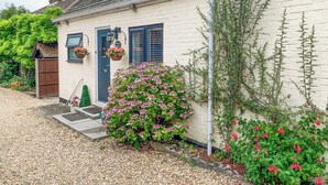 A quaint white cottage with a blue door, a small garden with pink flowers, and a wooden gate. - 2 bedroom accommodation in Clanfield, near Petersfield (Clanfield, near Petersfield)