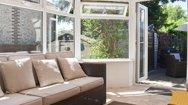 A sunlit room with a beige sofa, wicker furniture, and a view of greenery through large windows. - 2 bedroom accommodation in Clanfield, near Petersfield (Clanfield, near Petersfield)