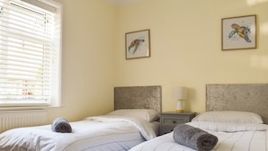 A room with two beds, each with striped bedding and rolled towels. There are two framed artworks on the walls, a window with blinds, and a bedside table with a lamp. - 2 bedroom accommodation in Clanfield, near Petersfield (Clanfield, near Petersfield)